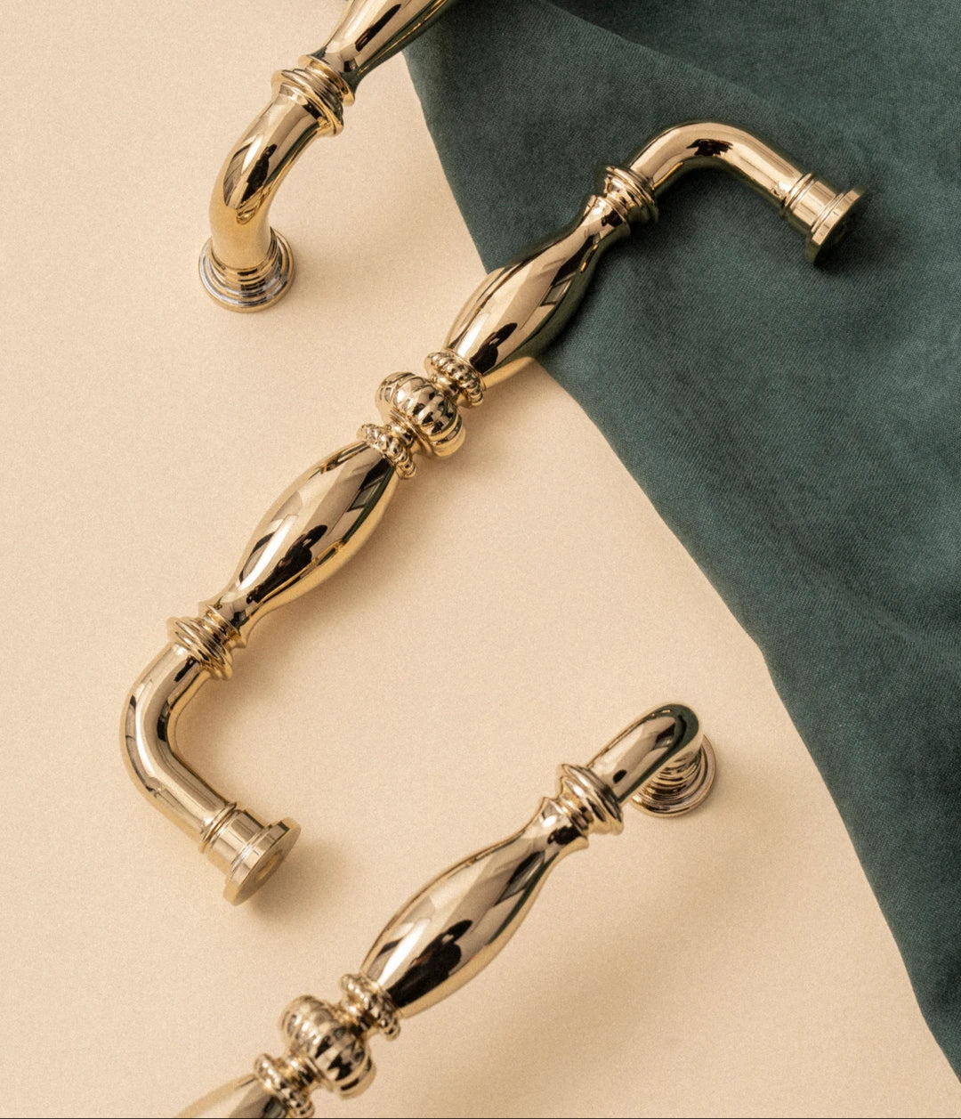 Goudkleurige luxe deurgrepen van Aurel op beige ondergrond met groene stof, modern en klassiek design